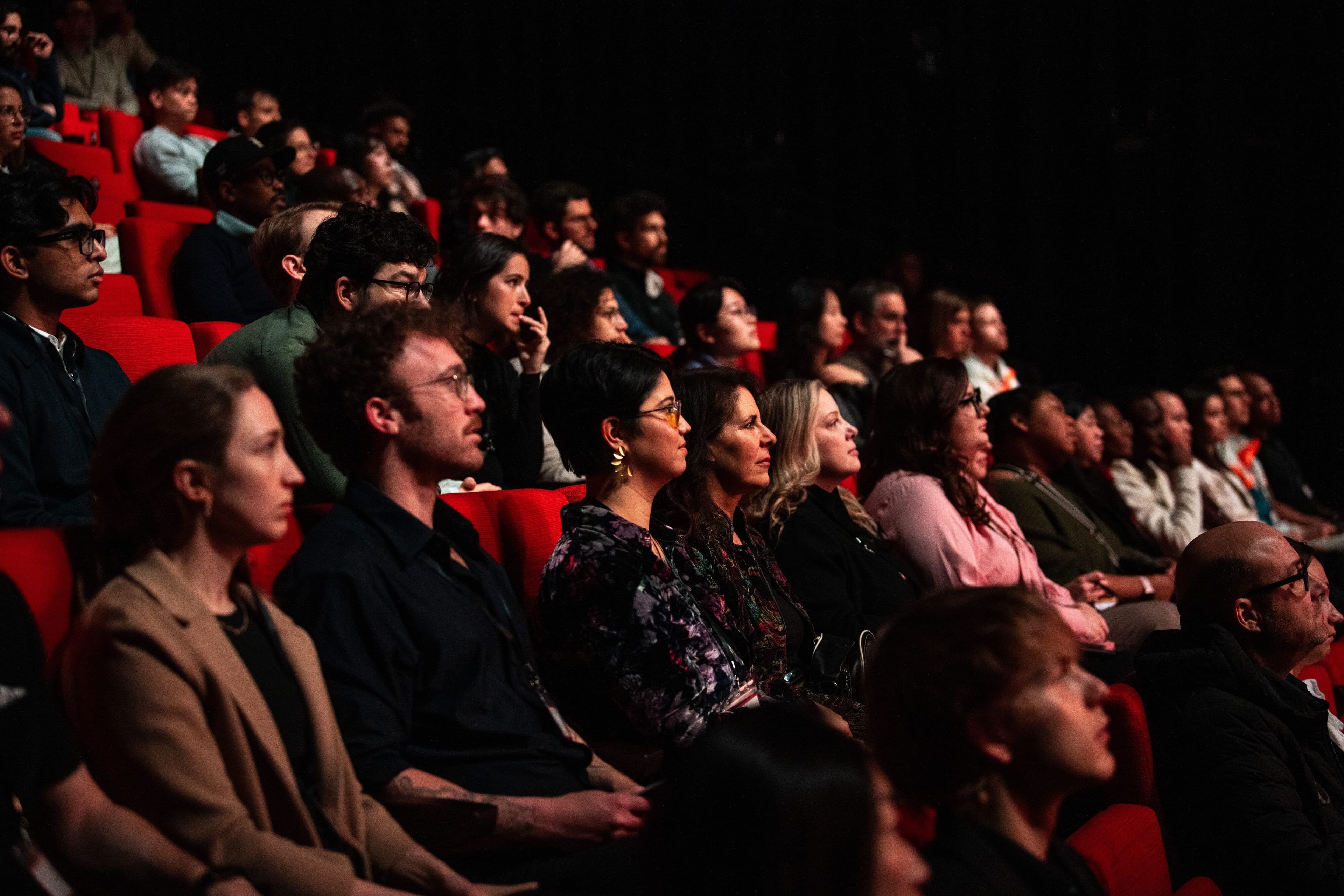 Audience members in red theater seats listen intently.